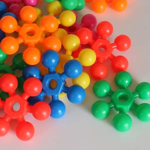 May include: A collection of colourful plastic star-shaped toys with six points. Each star has a central hole and is made of bright colours like red, orange, yellow, green, blue, and pink.