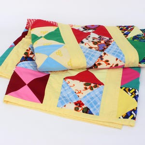 May include: A folded patchwork quilt with a variety of colorful fabric squares. The quilt features yellow, red, blue, green, and pink patches. The quilt is folded on a white surface.