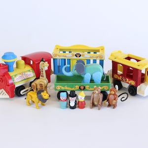 May include: A vintage Fisher-Price Circus Train toy set. The set includes a red and yellow train engine, two train cars, and several animal and circus performer figurines. The train cars are yellow, red, and green. The figurines include a giraffe, lion, elephant, bear, and monkey.