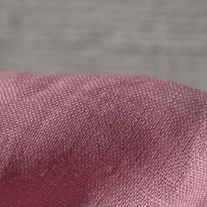 May include: Close-up of a soft, pink fabric with a textured weave. The fabric has a subtle sheen and a slightly wrinkled appearance.