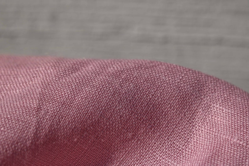 May include: Close-up of a soft, pink fabric with a textured weave. The fabric has a subtle sheen and a slightly wrinkled appearance.