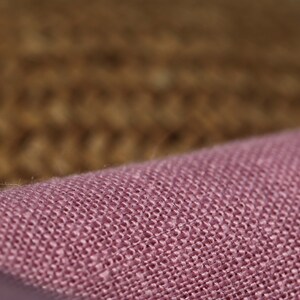 May include: Close-up of a pink woven fabric with a textured surface. The fabric has a subtle sheen and a slightly rough feel.