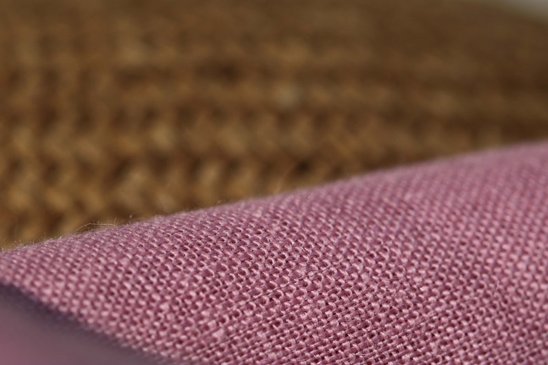 May include: Close-up of a pink woven fabric with a textured surface. The fabric has a subtle sheen and a slightly rough feel.