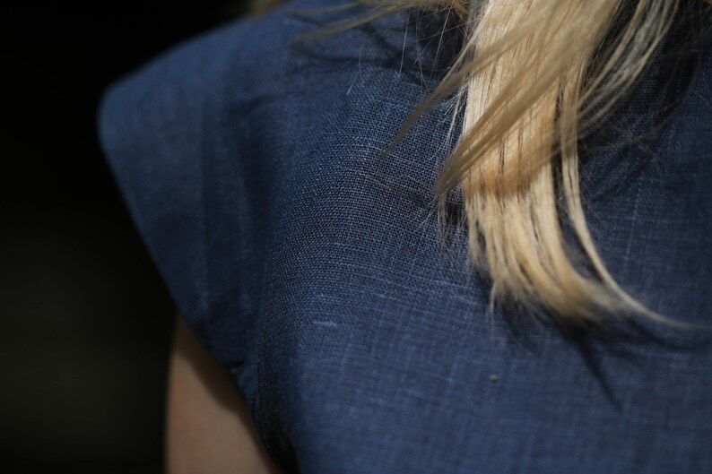 May include: Close-up of a dark blue linen fabric with a textured weave. The fabric is smooth and has a subtle sheen.