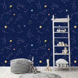 May include: Navy blue wallpaper with a constellation design in white, complemented by colorful planets. A white ladder displays toys like a wooden car, blocks, and a teddy bear. A black and white striped ottoman and a grey bunny toy are in the foreground, creating a playful scene.