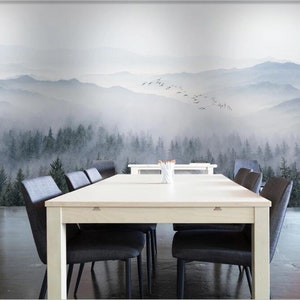 Puede incluir: Una mesa blanca con seis sillas negras se encuentra frente a un mural de pared que representa un bosque brumoso y monta&ntilde;as. El mural presenta una bandada de p&aacute;jaros volando sobre las monta&ntilde;as.