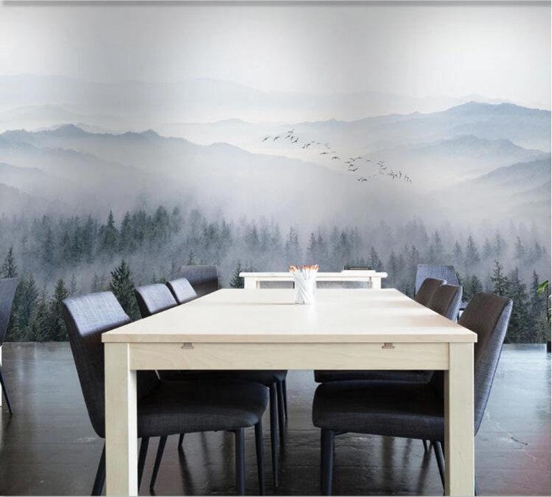 Puede incluir: Una mesa blanca con seis sillas negras se encuentra frente a un mural de pared que representa un bosque brumoso y monta&ntilde;as. El mural presenta una bandada de p&aacute;jaros volando sobre las monta&ntilde;as.