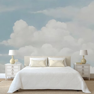 May include: A white bed with white bedding and two white pillows sits in front of a wall with a mural of a blue sky and white clouds.