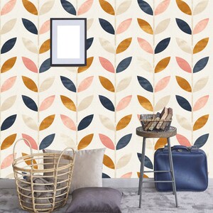 May include: A room with a white wall featuring a repeating pattern of stylized leaves in pink, blue, and gold. The wall has a framed picture, a wicker basket, a stool with a basket on top, and a blue suitcase.