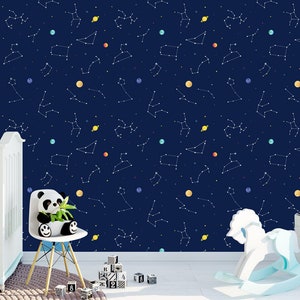 May include: Navy blue wallpaper with a constellation design, featuring white lines and colourful planets. A white cot, panda bear plush, rocking horse, and building blocks are in the foreground, suggesting a nursery theme.