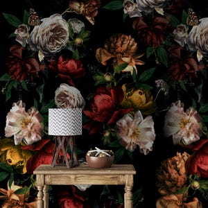 Puede incluir: Una mesa de madera con una lámpara y un cuenco con objetos decorativos sobre un fondo de papel pintado floral. La lámpara tiene una pantalla con un patrón de chevron gris y blanco. El papel pintado presenta grandes flores coloridas en tonos rojos, amarillos y crema.