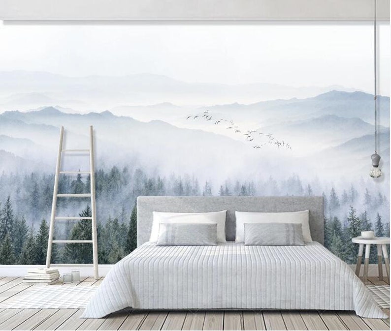 Puede incluir: Una cama blanca con un edred&oacute;n gris y dos almohadas blancas se encuentra frente a un mural de pared que representa un bosque brumoso y monta&ntilde;as. Una escalera de madera se apoya en la pared a la izquierda de la cama.