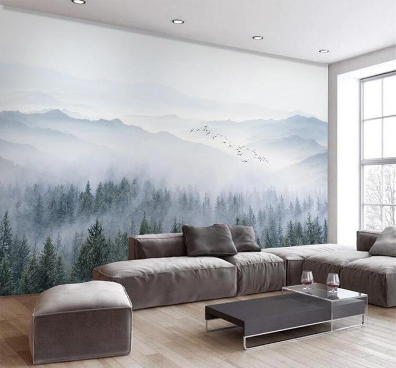Puede incluir: Una sala de estar con un sof&aacute; seccional gris y una mesa de caf&eacute; frente a un mural de pared que representa un bosque brumoso con una cordillera en el fondo.
