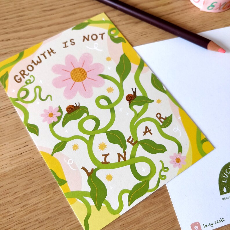 May include: A greeting card with the text "GROWTH IS NOT LINEAR" in a whimsical design. The card features a pink flower, green vines, and small snails. A blank white card and a colored pencil are in the background.
