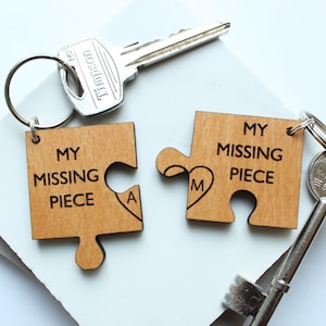 Puede incluir: Dos piezas de rompecabezas de madera con forma de corazón con el texto "My Missing Piece" en cada pieza. Las piezas están unidas a un llavero plateado con una llave plateada.