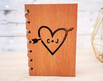 May include: A small wooden journal with a heart and arrow design. The heart has the initials "C + J" inside. The journal is bound with twine.