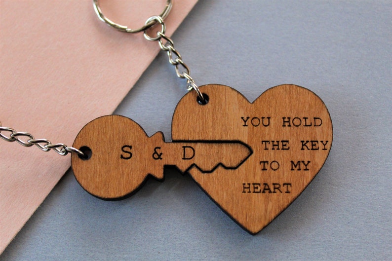 Pode incluir: Chaveiros de madeira com design de chave e cora&ccedil;&atilde;o. A chave tem as iniciais "S & D" e o cora&ccedil;&atilde;o diz "YOU HOLD THE KEY TO MY HEART". O chaveiro &eacute; preso a uma corrente e um anel prateados.