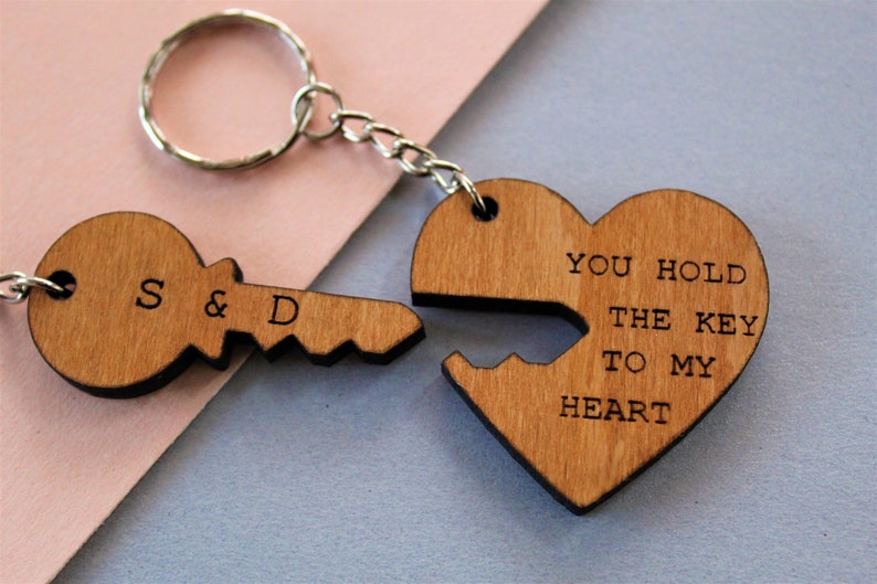 Pode incluir: Chaveiros de madeira com design de chave e cora&ccedil;&atilde;o. A chave &eacute; gravada com "S & D", e o cora&ccedil;&atilde;o diz "YOU HOLD THE KEY TO MY HEART". Os chaveiros s&atilde;o conectados por uma corrente e um anel de metal.
