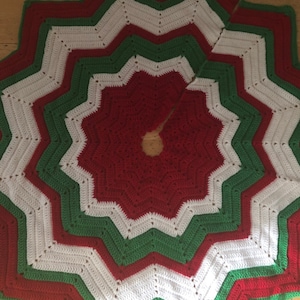 Op de afbeelding: Een rood, wit en groen gehaakte kerstboomrok met een stervormig patroon.