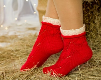 May include: Red knitted ankle socks with white lace trim. The socks have a delicate openwork pattern and are shown on a pair of legs.