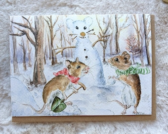 Könnte beinhalten: Zwei Mäuse in einem verschneiten Wald bauen einen Schneemann. Eine Maus trägt einen roten Schal und hält eine Schaufel, während die andere einen grünen Schal trägt. Der Schneemann hat ein weißes Gesicht und eine Karottennase.