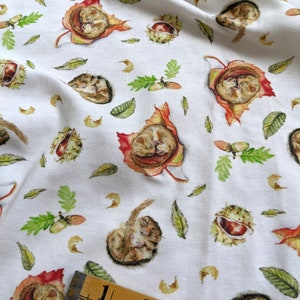May include: White fabric with a repeating pattern of sleeping dormice curled up in autumn leaves and chestnuts. The fabric is measured with a wooden ruler.