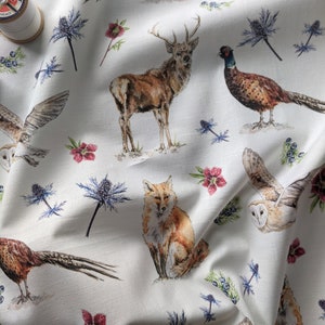 May include: White fabric with a repeating pattern of woodland animals, including a fox, deer, owl, and pheasant. The fabric also features blue flowers and red berries.