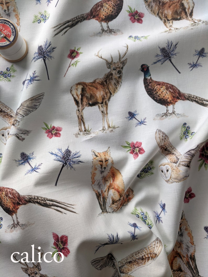 May include: White fabric with a repeating pattern of woodland animals, including a fox, deer, owl, and pheasant. The fabric also features blue flowers and red berries.
