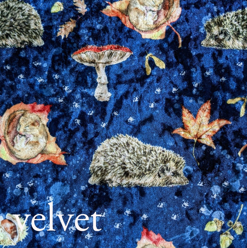 May include: Blue velvet fabric with a repeating pattern of hedgehogs, mushrooms, and autumn leaves. The fabric has a subtle texture and the word "velvet" is printed in white at the bottom of the image.