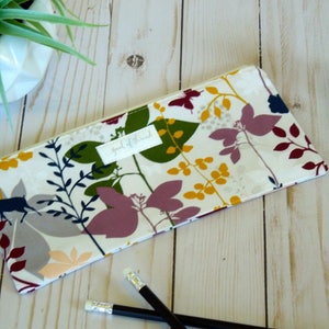May include: A white zippered pouch with a floral print featuring a deer, leaves, and branches in shades of red, green, blue, yellow, and gray. The pouch has a label that reads "speak of the mind".
