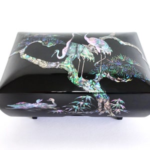 May include: A black wooden jewelry box with a mother-of-pearl inlay design of cranes and trees. The box has a hinged lid and is decorated with intricate details.
