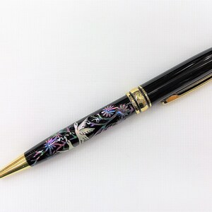 May include: Black ballpoint pen with gold accents. The pen features a decorative band with a floral and bird design in iridescent colors. The pen's tip and clip are gold-colored.