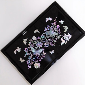 Könnte beinhalten: Ein schwarzes rechteckiges Tablett mit einem dekorativen Design aus Schmetterlingen und floralen Ranken aus irisierendem Perlmutt. Das Tablett ist perfekt zum Servieren von Snacks oder Getränken.