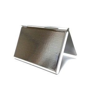 May include: A silver-colored business card holder with a textured surface. The holder is in a triangular shape, with a hinged top and a reflective finish. The design is simple and modern, suitable for professional use.