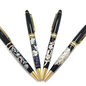 Könnte beinhalten: Vier schwarze Stifte mit goldenen Akzenten und aufwendigen floralen Designs. Die Stifte haben goldene Spitzen und Clips. Die floralen Muster sind in Weiß, Silber und schillernden Farben gehalten. Die Stifte sind fächerförmig angeordnet.
