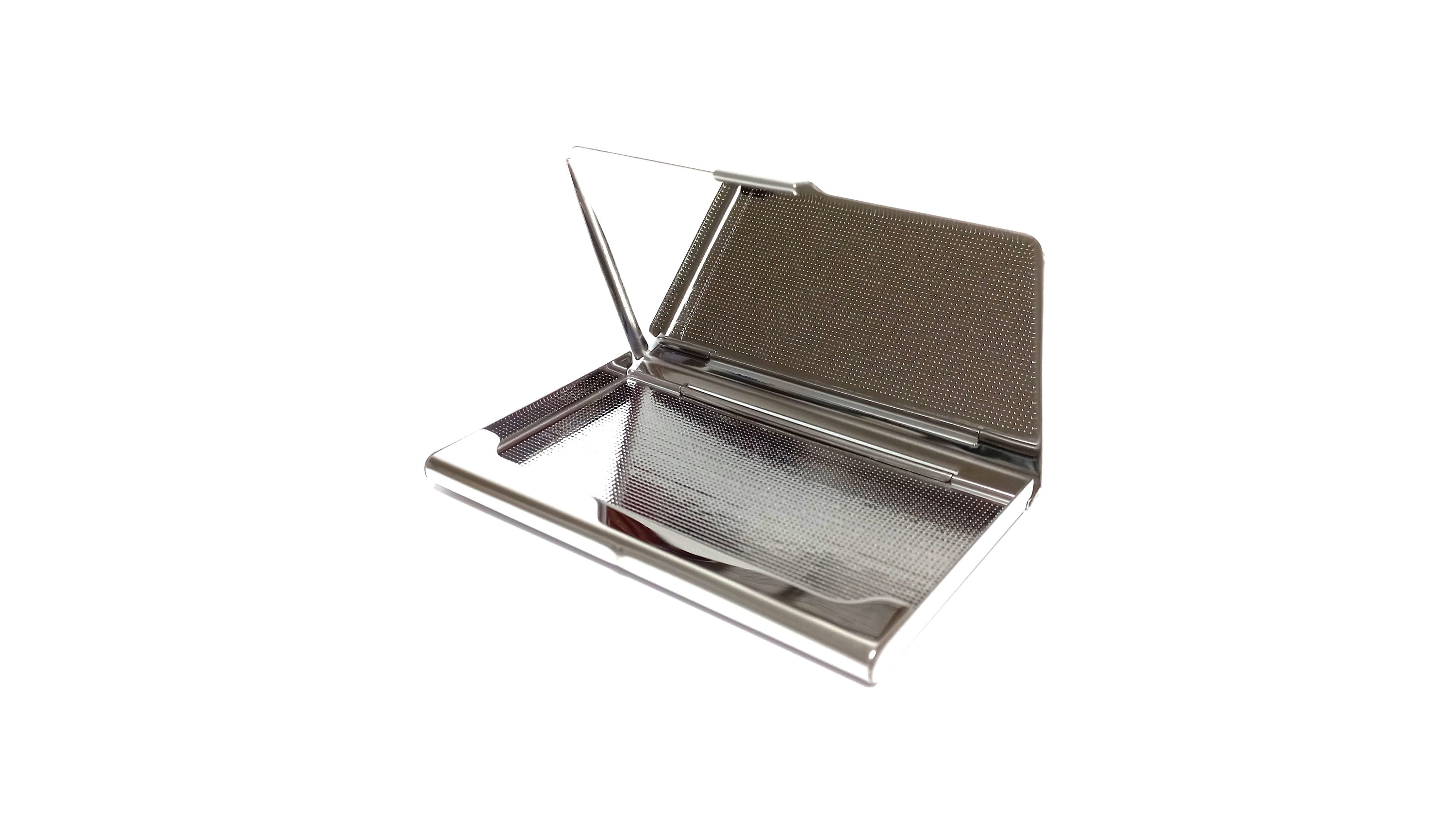 May include: A silver-colored business card holder, open to display the interior. The interior has a textured, dark gray surface on the top half and a shiny, reflective surface on the bottom half. The lid is slightly ajar.