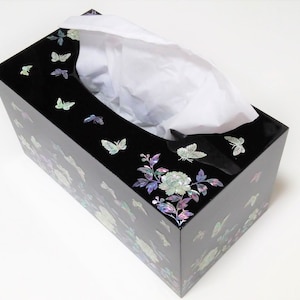 May include: Black tissue box cover with a floral design featuring butterflies and a rose. The design is made of mother of pearl inlay.
