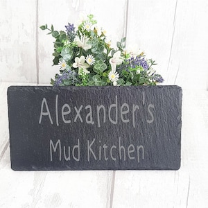 May include: Black slate sign with the text "Alexander's Mud Kitchen" etched in white.