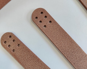 Peut inclure: Deux lanières en cuir brun avec plusieurs trous pour ajuster la longueur. Les lanières sont en cuir texturé et ont un aspect rustique.