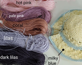 May include: A collection of colorful yarn skeins in shades of hot pink, pale pink, coral, lilas, and dark lilas. A crocheted hat in yellow and milky blue is also visible. The image is ideal for craft projects.