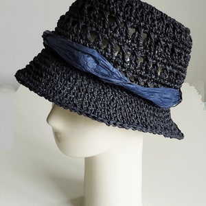 May include: A navy blue crocheted sun hat with a blue ribbon tied around the crown. The hat is on a white mannequin head.