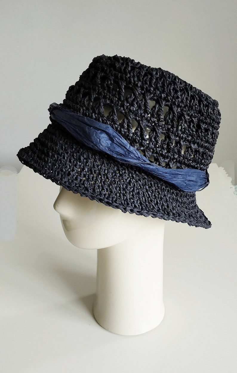 May include: A navy blue crocheted sun hat with a blue ribbon tied around the crown. The hat is on a white mannequin head.