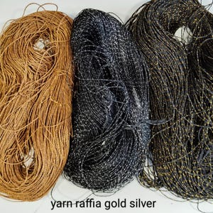 Puede incluir: Tres carretes de hilo, uno marrón, uno negro con destellos plateados y uno negro con destellos dorados. El hilo está etiquetado como "yarn-raffia gold silver".