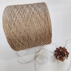 Könnte beinhalten: Ein Knäuel naturbraunen Garns, zu einer Kugel geformt. Das Garn besteht aus einer Mischung aus Leinen und Baumwolle und hat einen dezenten Glanz. Das Garn ist perfekt zum Stricken oder Häkeln.