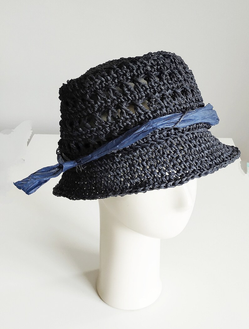 May include: A black crocheted hat with a blue ribbon tied around the crown. The hat is sitting on a white mannequin head.