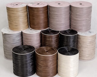 May include: A collection of twelve cylindrical spools of raffia ribbon arranged in three rows. The spools feature a variety of neutral earth tones including shades of beige, tan, brown, grey, black, and off-white, each with a textured surface.