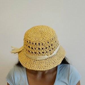 May include: A light yellow crocheted sun hat with a white ribbon around the crown. The hat is made of a lightweight material and has a wide brim.