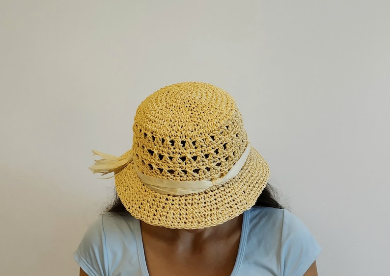 May include: A light yellow crocheted sun hat with a white ribbon around the crown. The hat is made of a lightweight material and has a wide brim.