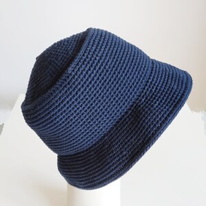 May include: A dark blue crocheted bucket hat. The hat is made of a thick, textured yarn and has a wide brim.