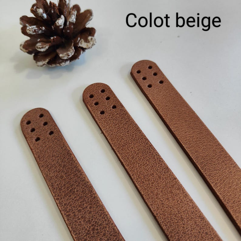 K&ouml;nnte beinhalten: Drei braune Lederriemen mit L&ouml;chern zum N&auml;hen. Die Riemen sind horizontal auf einer wei&szlig;en Oberfl&auml;che angeordnet. Der Text "Colo beige" ist in der oberen rechten Ecke des Bildes sichtbar.